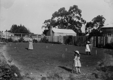 Two young girls and a woman playing croquet