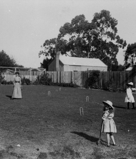 Two young girls and a woman playing croquet