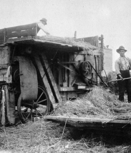 Workmen feeding hay into a threshing mill