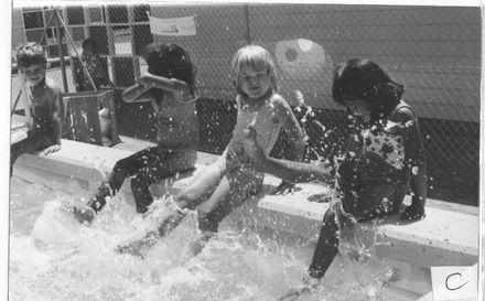 Children sitting on side of swimming pool splashing