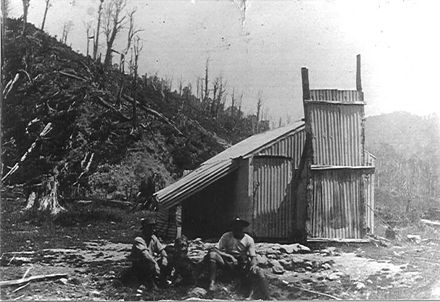 Corrugated iron hut and two men (unidentified)