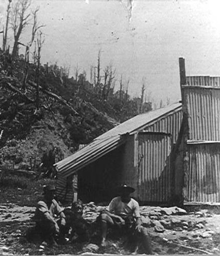 Corrugated iron hut and two men (unidentified)