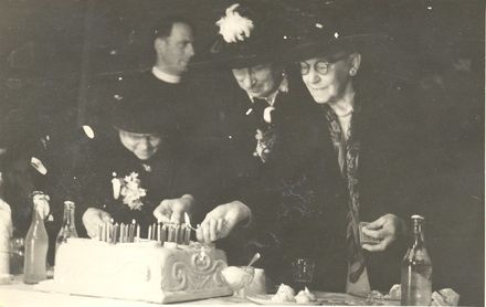 3 elderly women, including Mrs Lett, lighting candles on a cake.