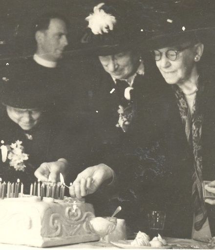3 elderly women, including Mrs Lett, lighting candles on a cake.