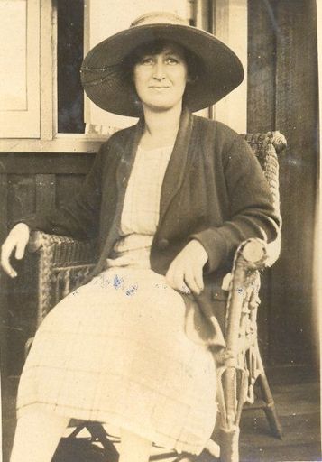 Woman wearing large hat sitting in wicker chair outside window