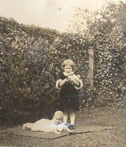 Young girl and baby on blanket in front of hedge