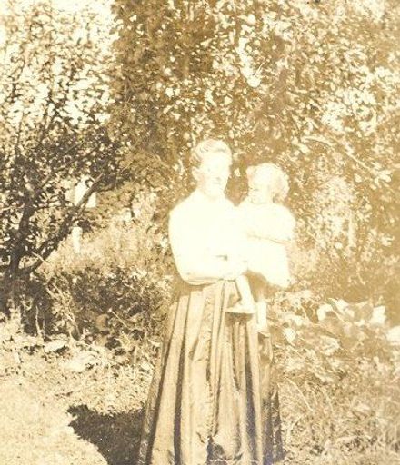 Woman holding young child in front of trees