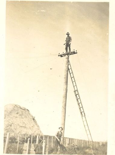 Tom Sunley standing on top of power pole during wire stringing, c.1920's-30's