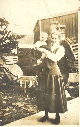 Woman holding young child in front of boxes and shed