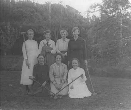 Seven young women with croquet mallets on lawn
