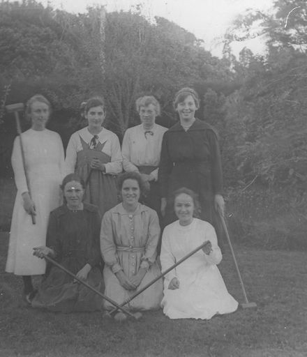 Seven young women with croquet mallets on lawn