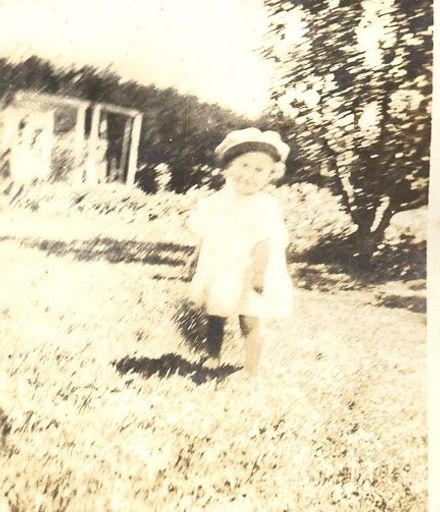 Young girl wearing hat in front of trees and shed