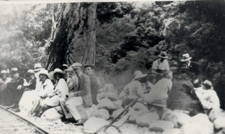 Group (unidentified) men & women sitting on rocks beside bush tramline, c.1930's