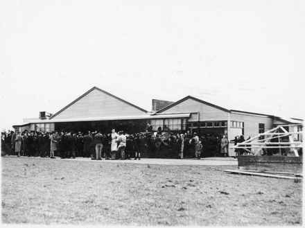 Large gathering in front of corrugated iron hanger